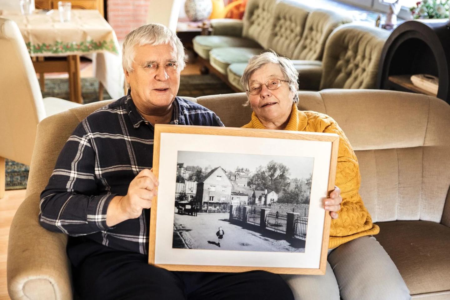 Ein Ehepaar sitzt auf dem Sofa und hält ein Foto ihrer Immobilie in den Händen.
