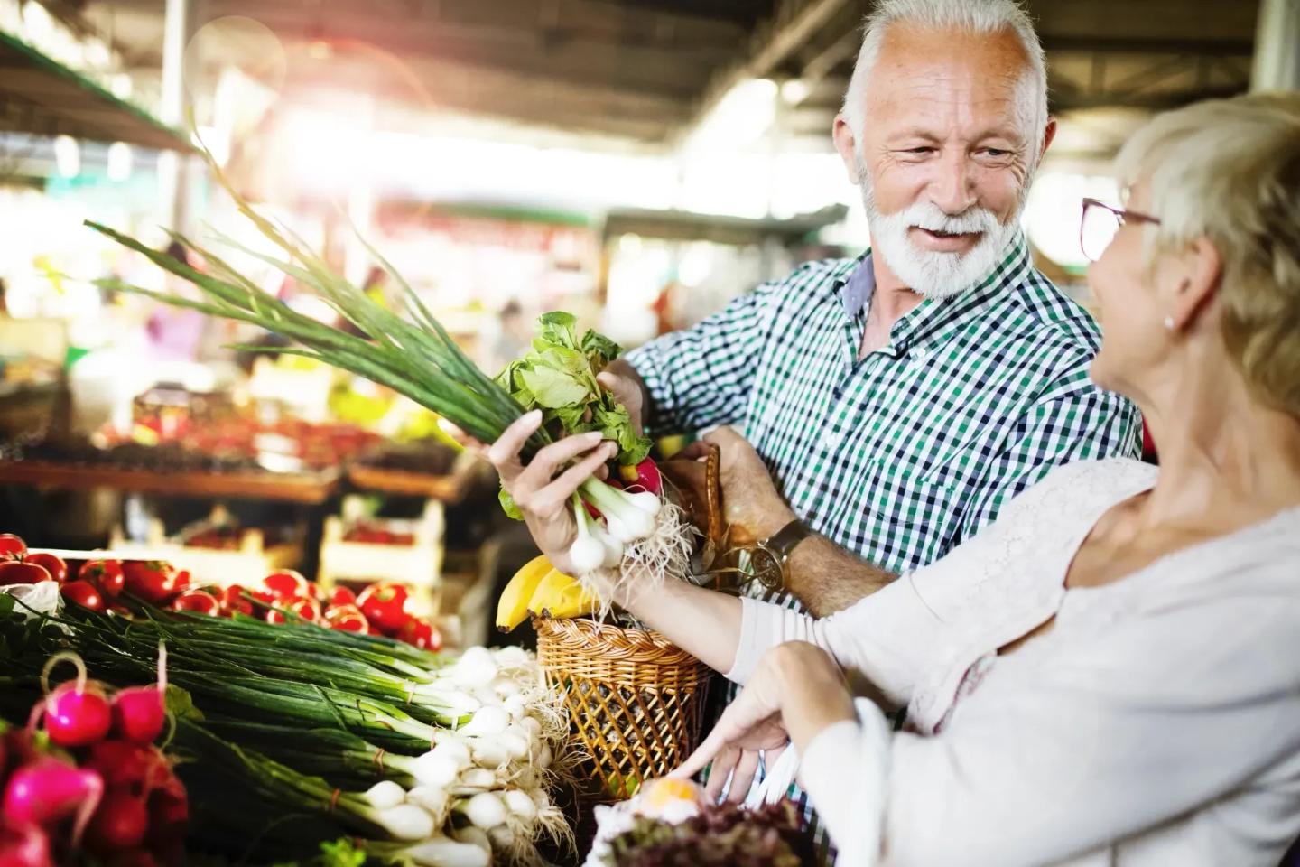 Ein Ehepaar steht auf einem Markt und kauft Gemüse. Sie möchten sich gesund ernähren.