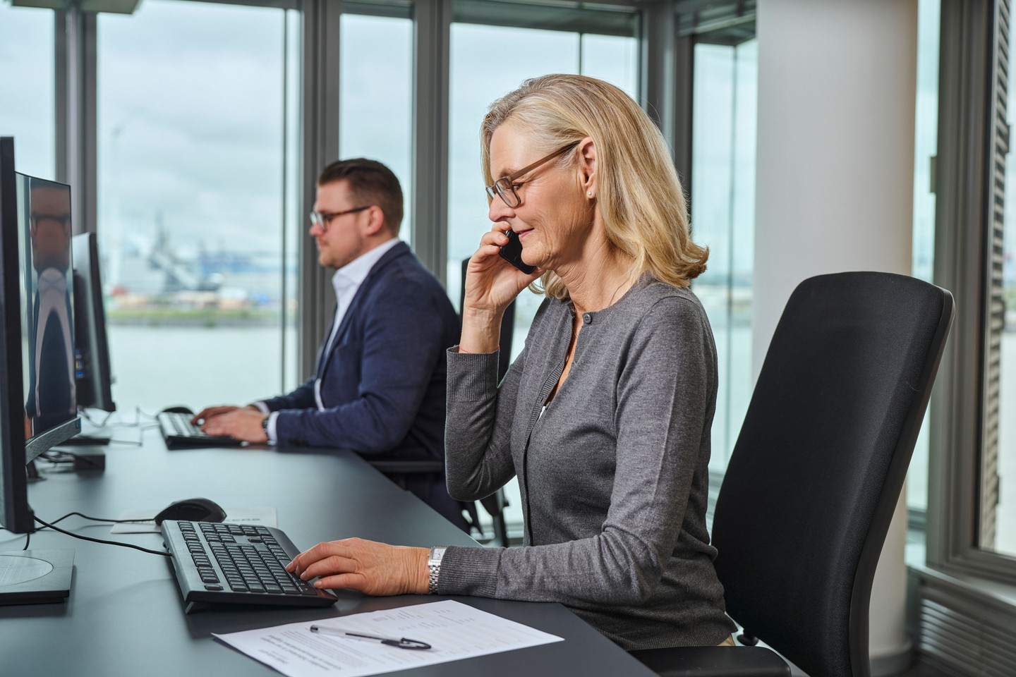 Zwei Mitarbeiter sitzen am Schreibtisch. Der Mann schaut runter, die Frau schaut in den Bildschirm ihres Computers.