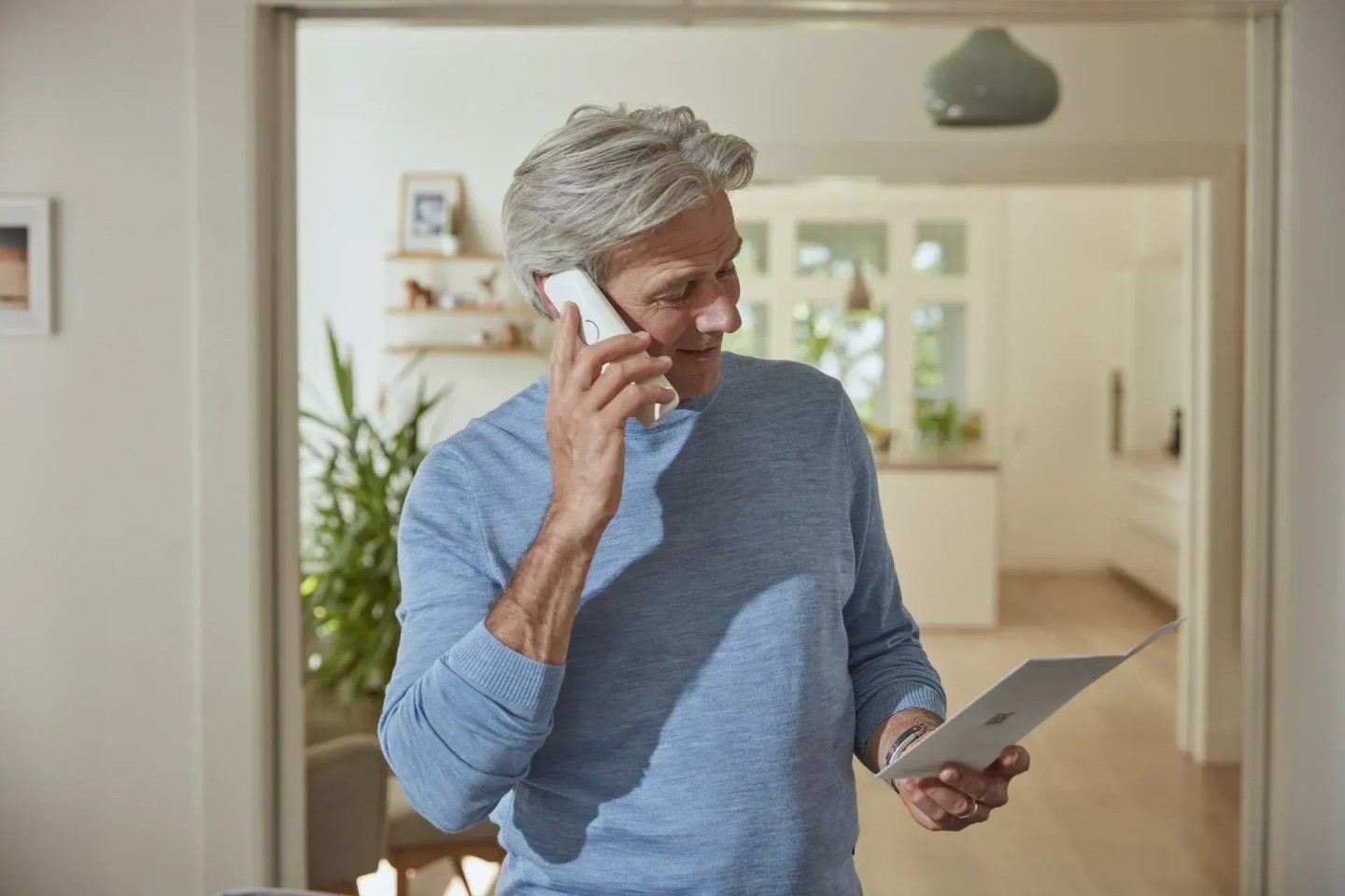 Ein Mann steht in der Küche und ist am Telefon. Er spricht über den Teilverkauf.