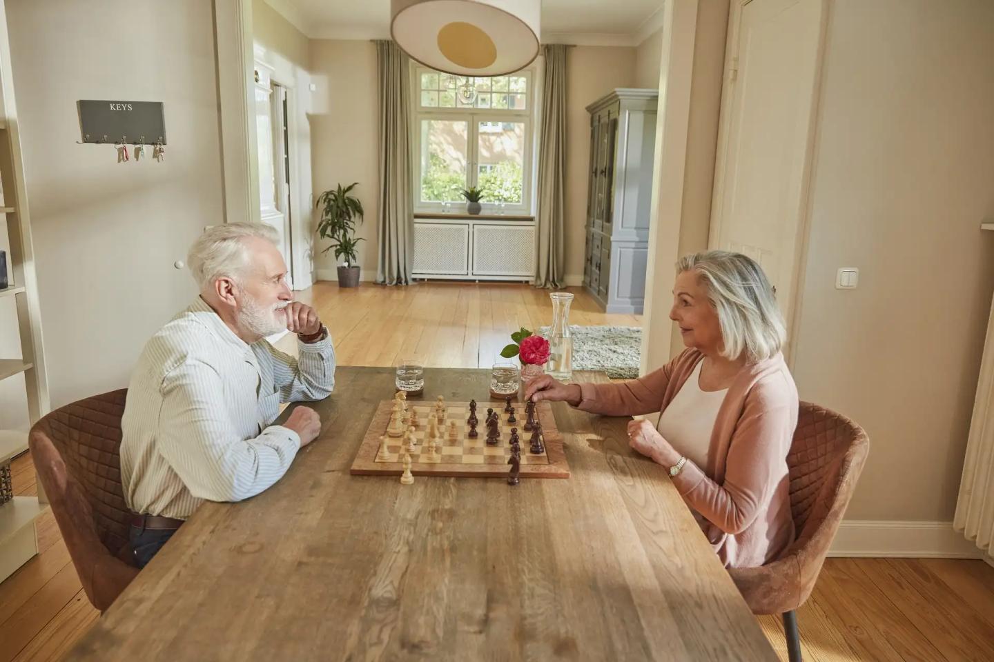 Ein Paar im Rentenalter sitzt sich an einem Tisch gegenüber und spielt Schach.