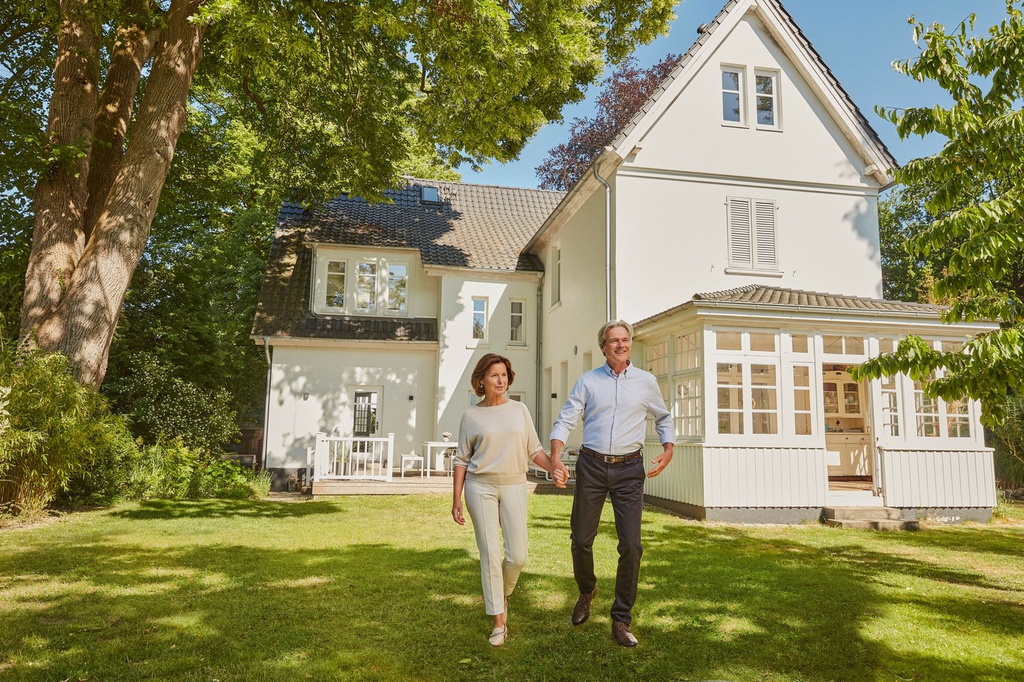 Ein Ehepaar geht im Garten vor ihrer Immobilie entlang. Sie lächeln.