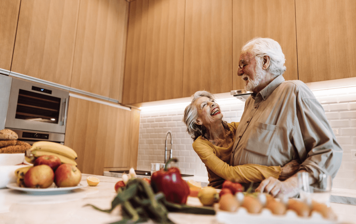 Paar in ihrer Küche. Die Frau umarmt den Mann. Beide lachen. Essen steht in der Küche.