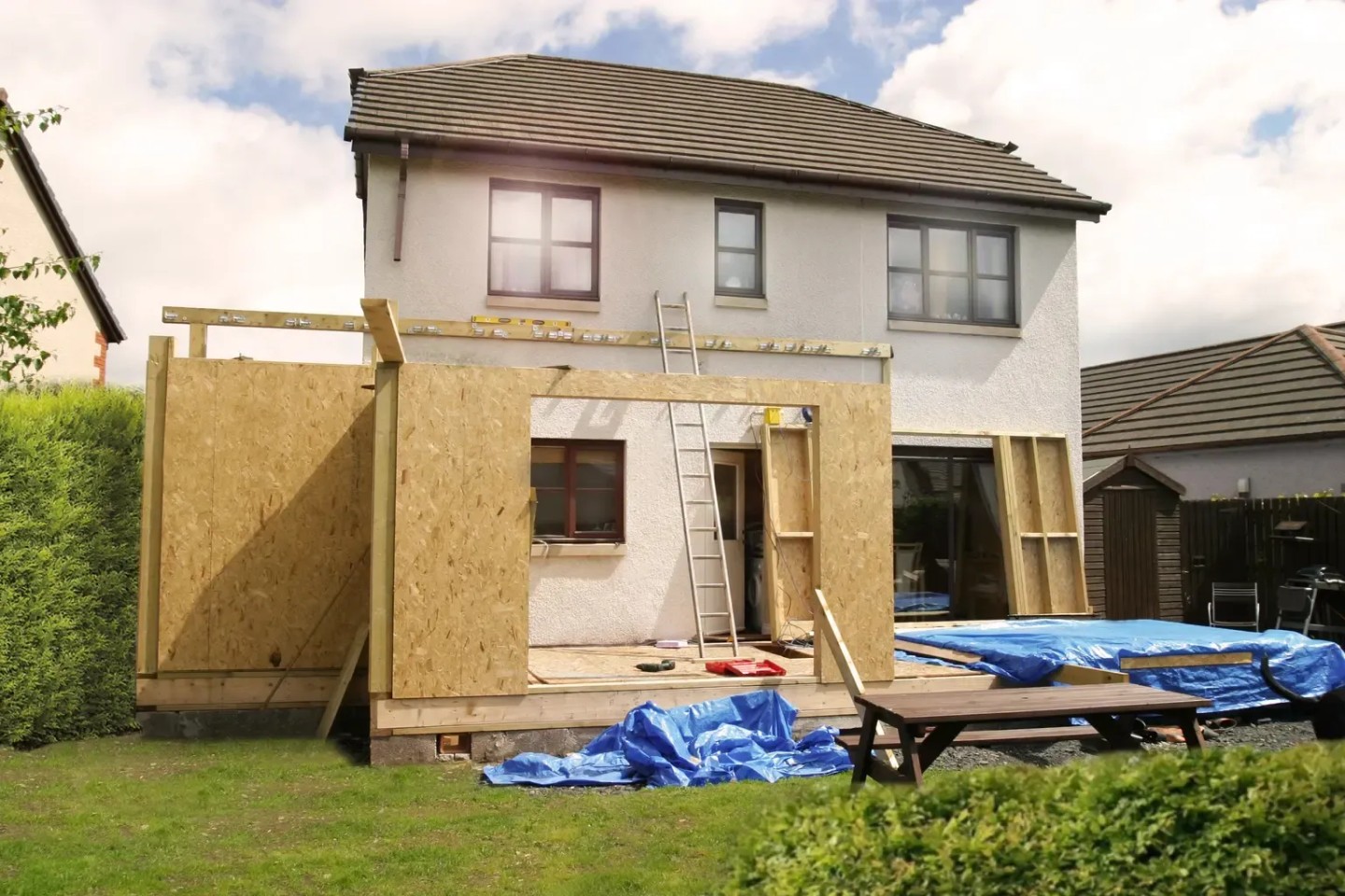 Ein Hausanbau an einer Immobilie. Es ist noch eine Baustelle mit Plane auf dem Boden und Holz überall.