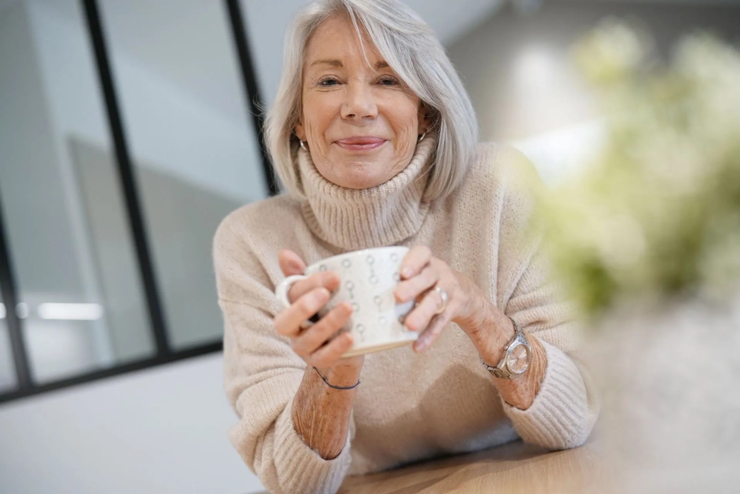 Eine Frau sitzt am Tisch und lächelt in die Kamera mit einer Tasse in den Händen. Sie spricht über die Rechte und Möglichkeiten bei Pflegebedürftigkeit.