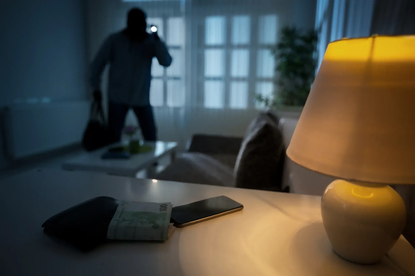 Eine dunkle Gestalt die einen Einbrecher darstellen soll ist in einem Wohnzimmer und hält eine Taschenlampe in der Hand.
