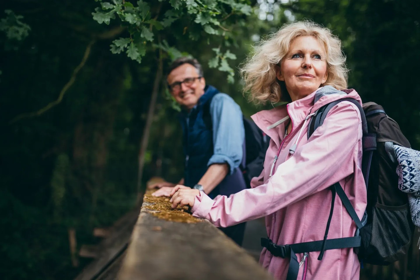 Zwei Senioren gehen wandern. Sie sind über ein Geländer gebeugt und stehen in einem Wald.