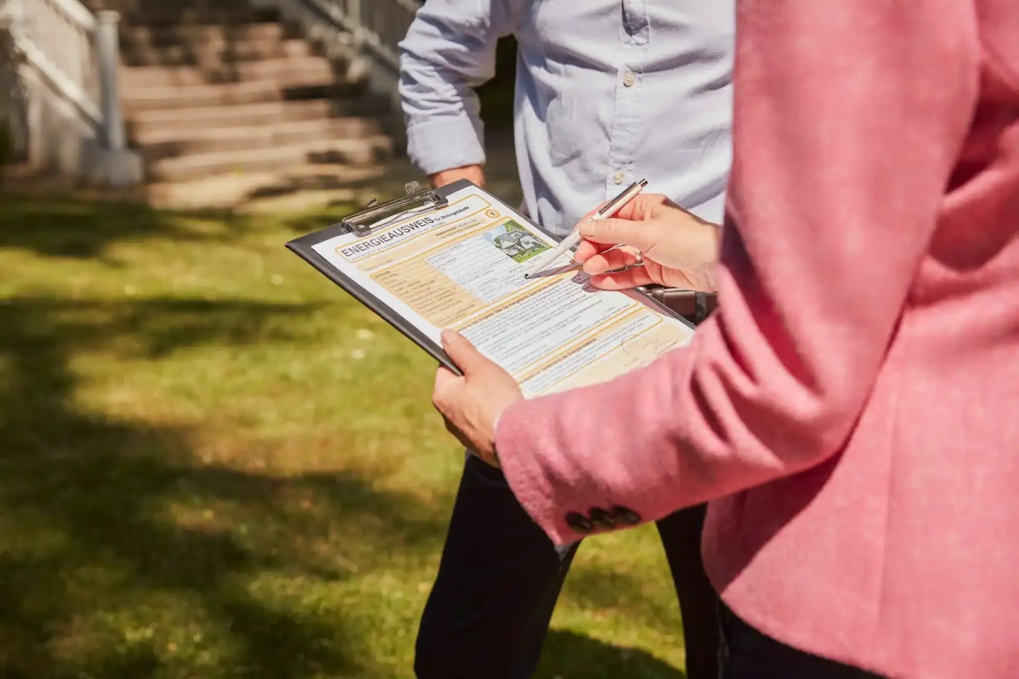 Eine Kundenberaterin steht mit ihren Kunden im Garten mit einem Clipboard in der Hand. Sie erklärt den Teilverkauf.
