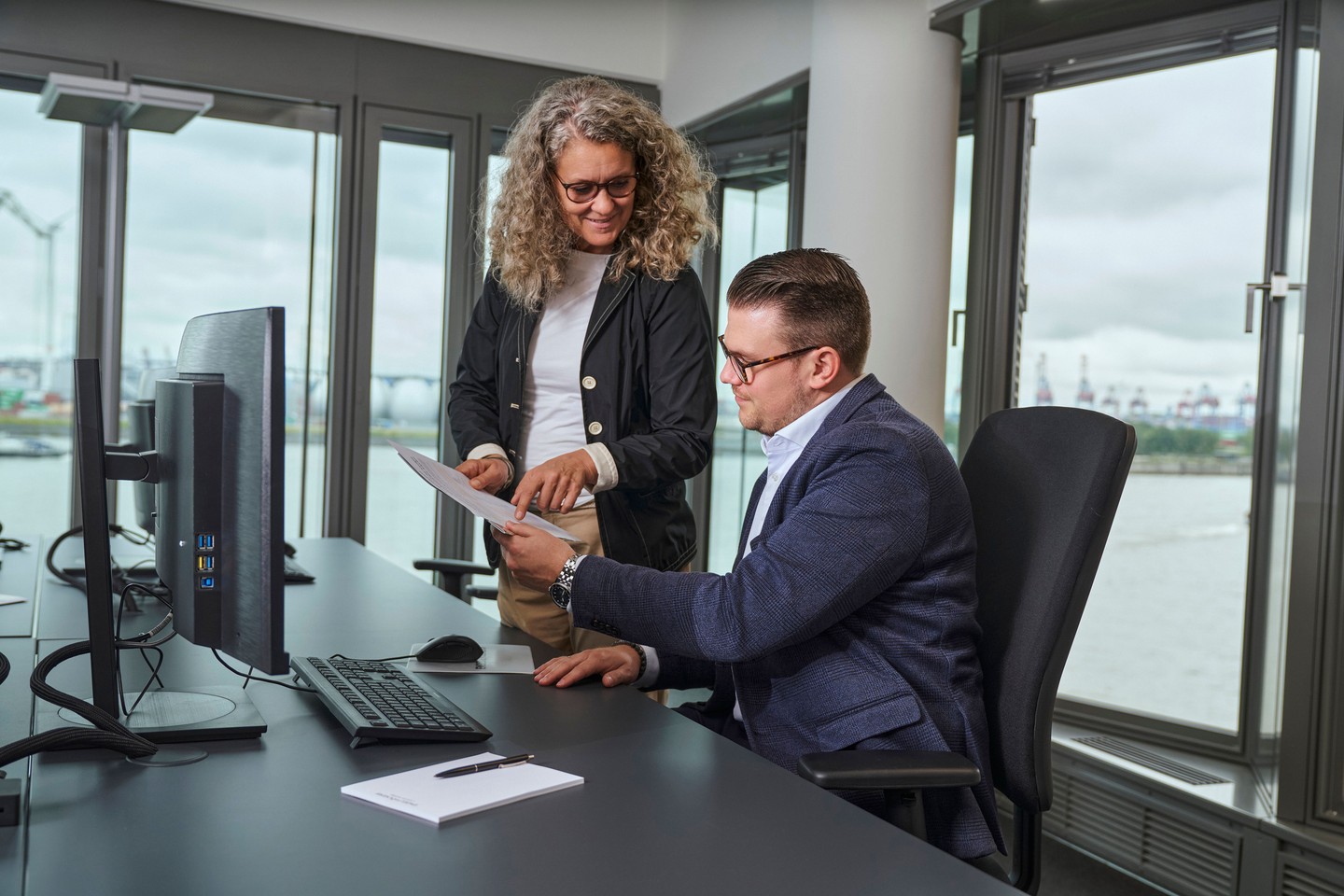 Zwei Mitarbeiter schauen auf Dokumente und sprechen miteinander.