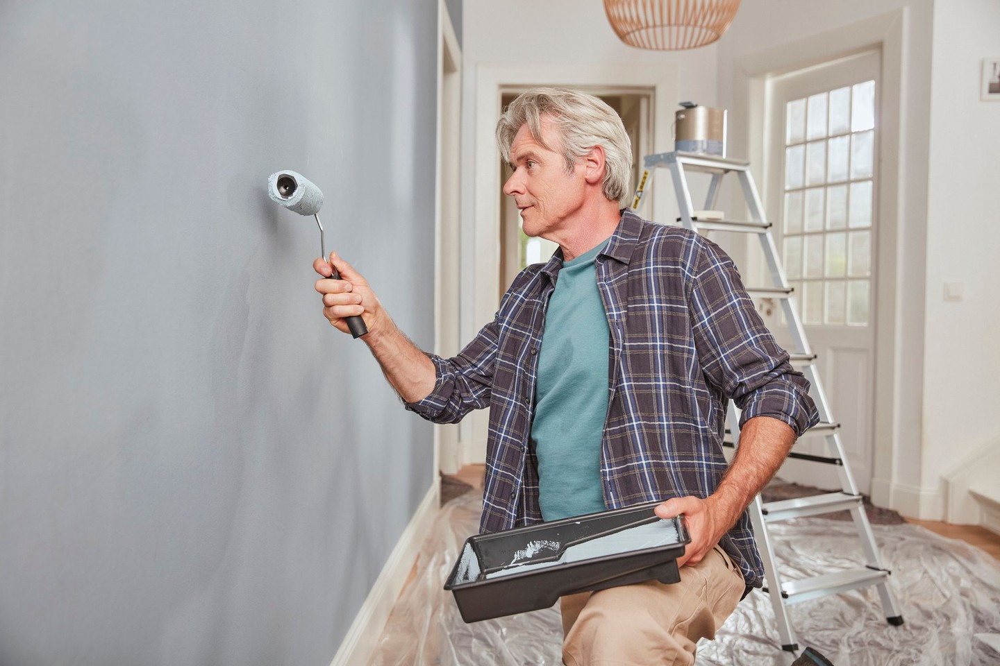 Ein Mann streicht die Wand seines Hauses in einer grauen Farbe.