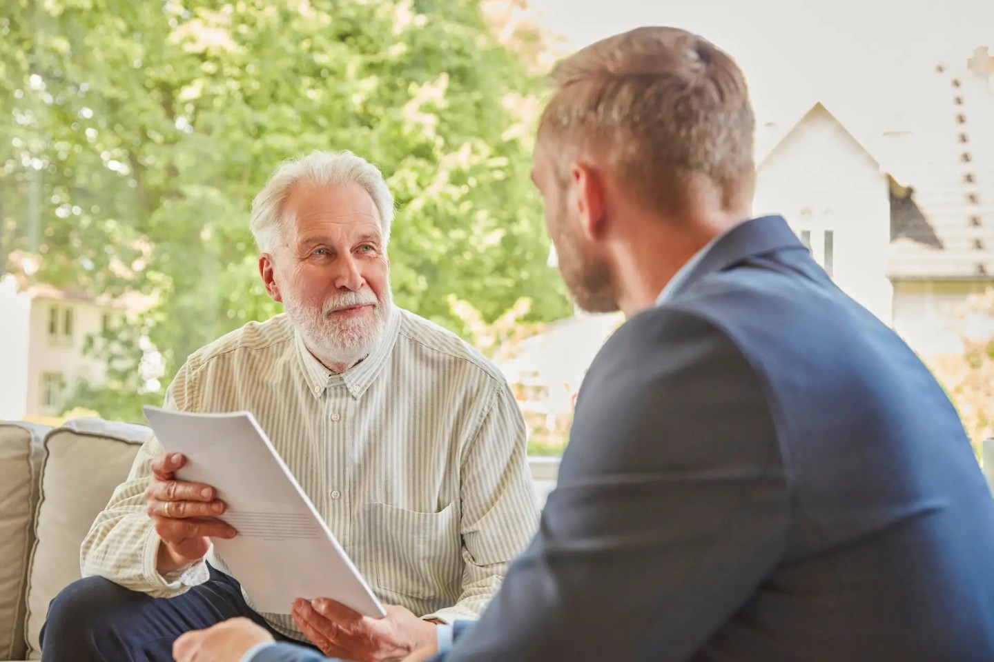 Ein Mann im Rentenalter sitzt einem jüngeren Mann im Anzug gegenüber und hält Unterlagen in seiner Händen.