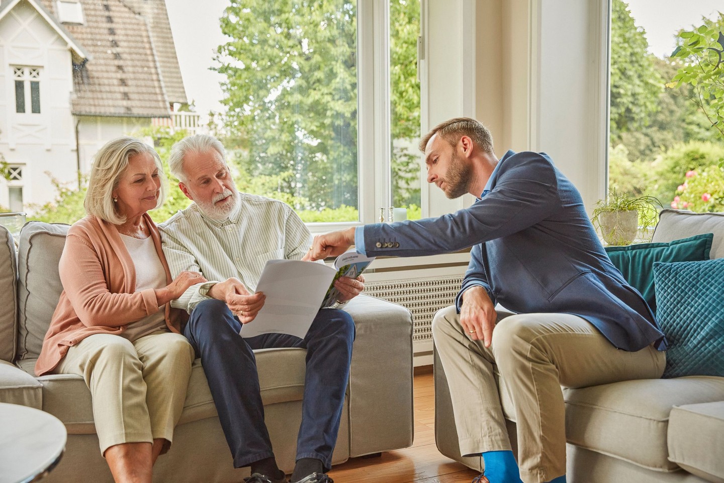 Ein Kundenberater sitzt auf dem Sofa und zeigt auf etwas in einer Broschüre die von einem Kunden gehalten wird.