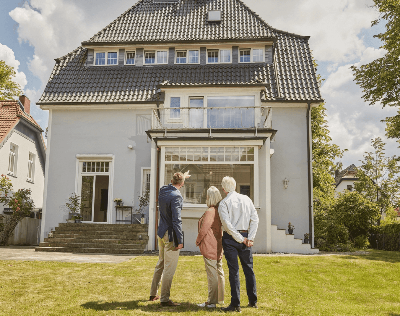 Ein Paar im Rentenalter steht gemeinsam mit einem jüngeren Mann vor einem Haus