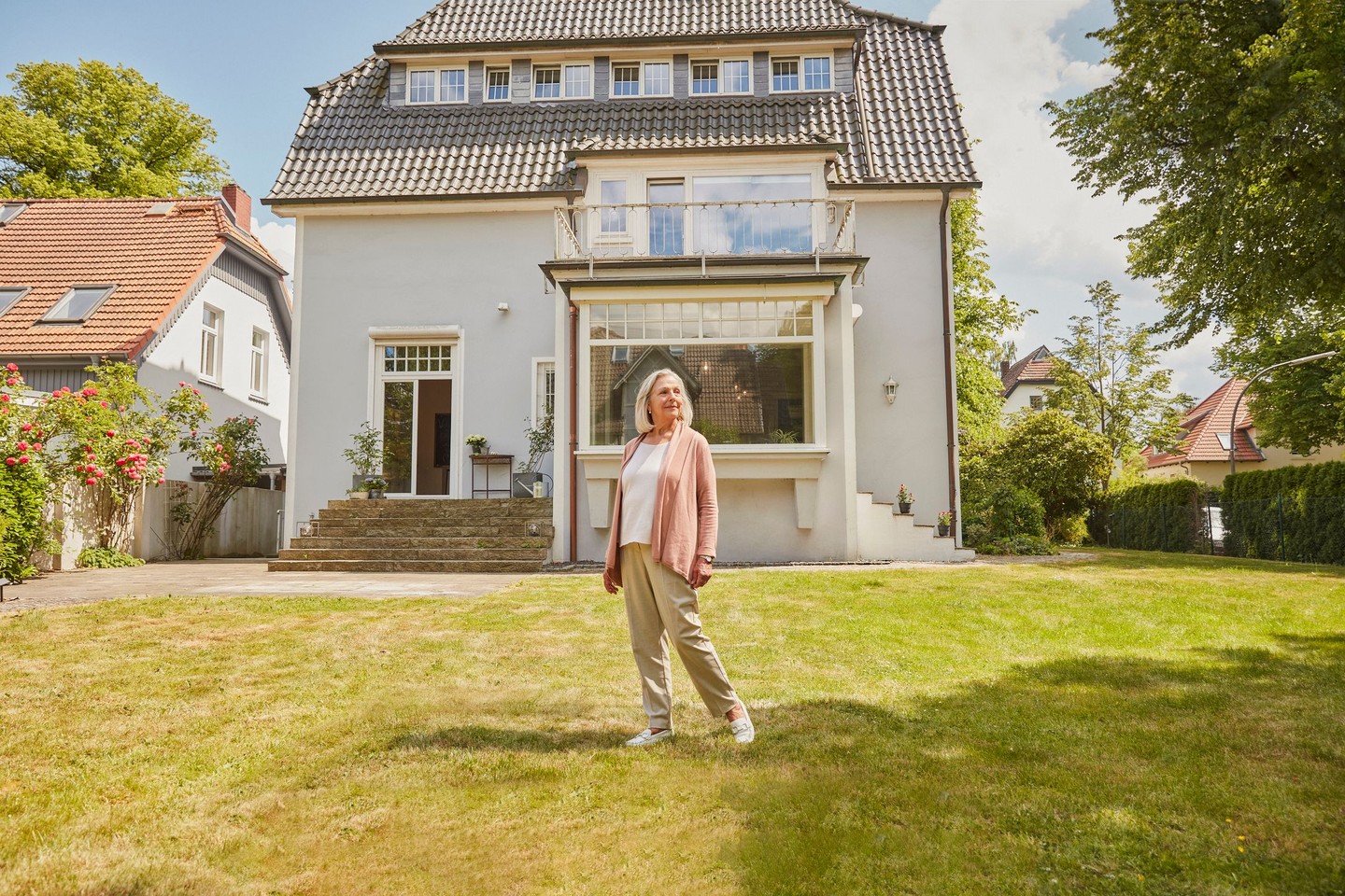 Eine Frau steht vor ihrer Immobilie im Garten.