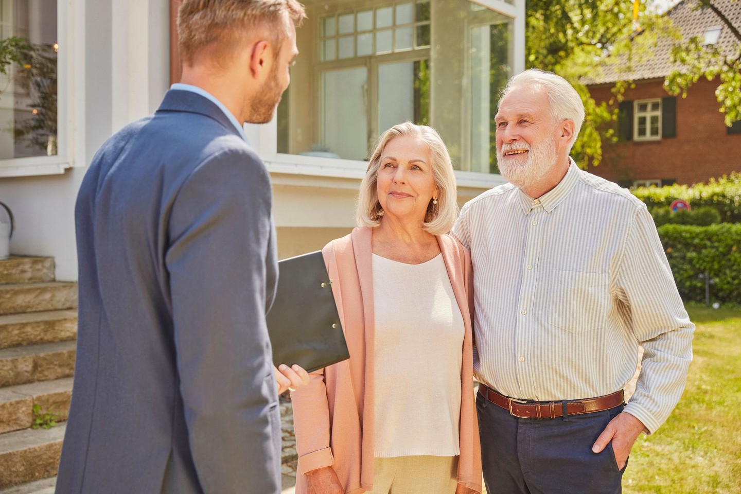 Ein Kundenberater steht mit zwei Kunden vor der Immobilie und spricht über den Teilverkauf.