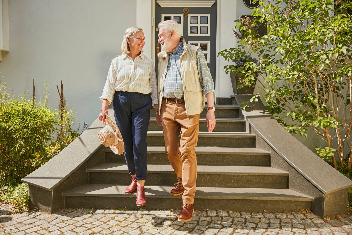 Ein Ehepaar geht die Treppe vor ihrem Haus runter und lächelt sich an.