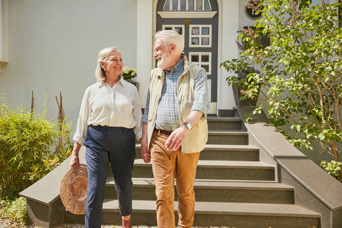 Ein Ehepaar geht die Treppe vor ihrem Haus runter und lächelt sich an.