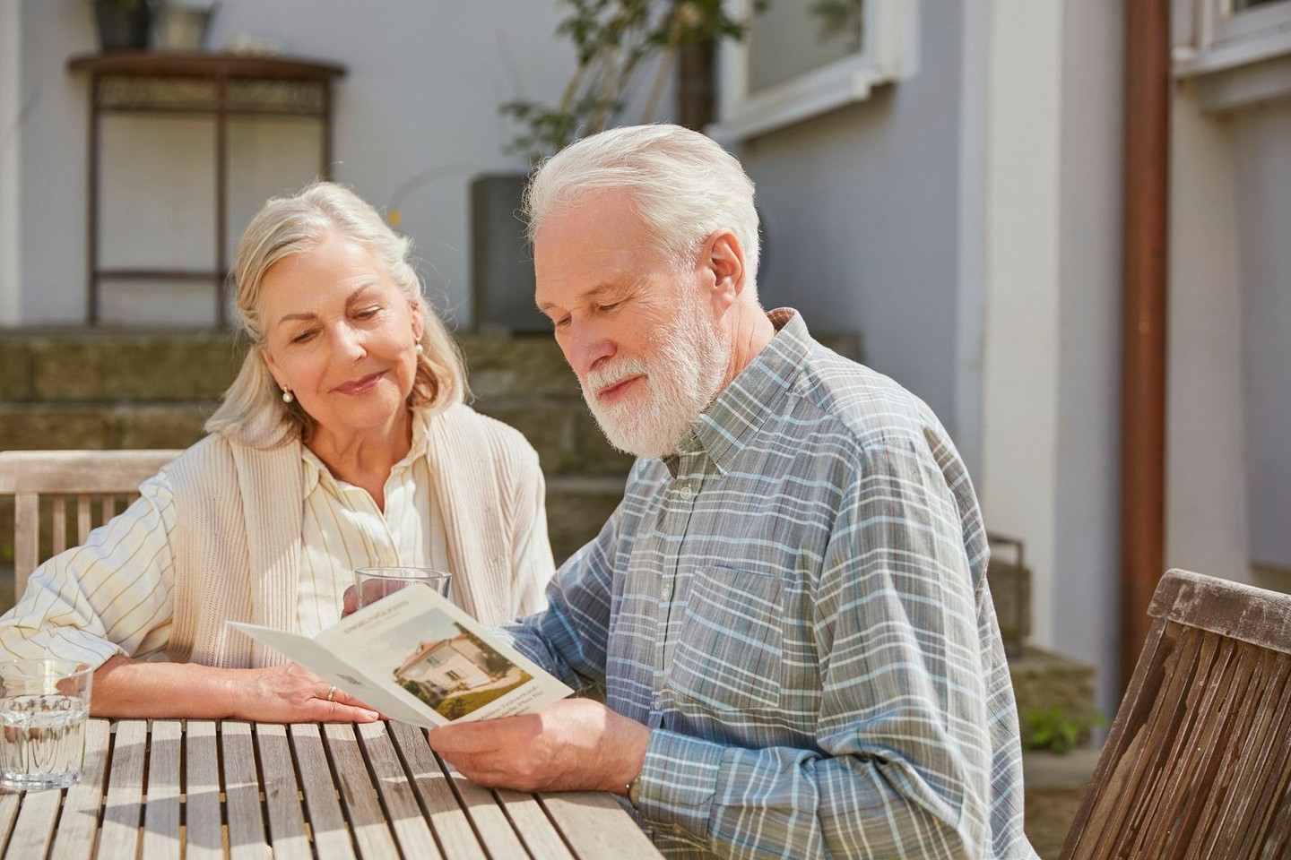 Ein älteres Ehepaar sitzt am Tisch und sie lesen einen Flyer.