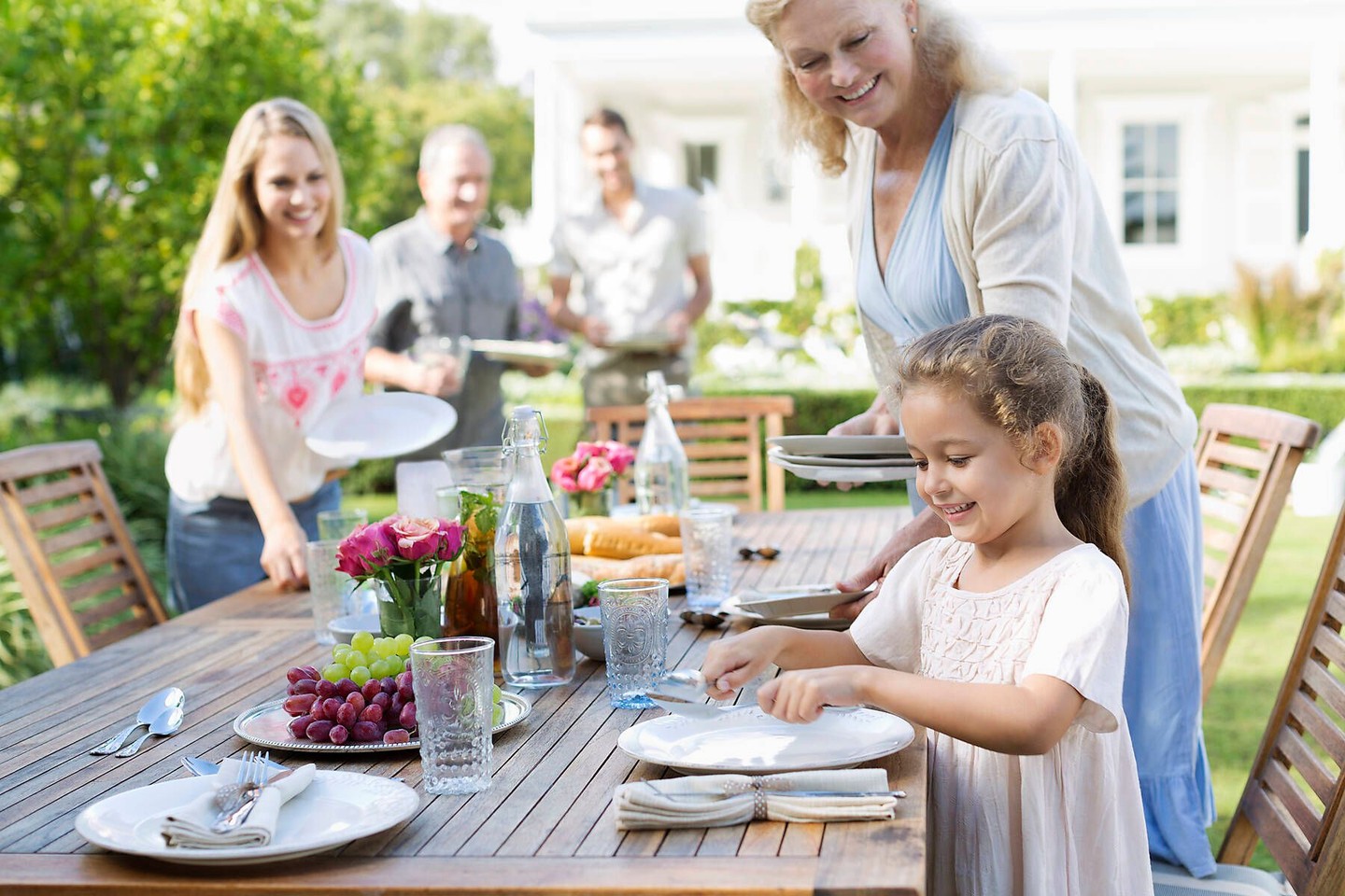 Eine Familie, Eltern, Kind und Grosseltern decken den Tisch im Garten