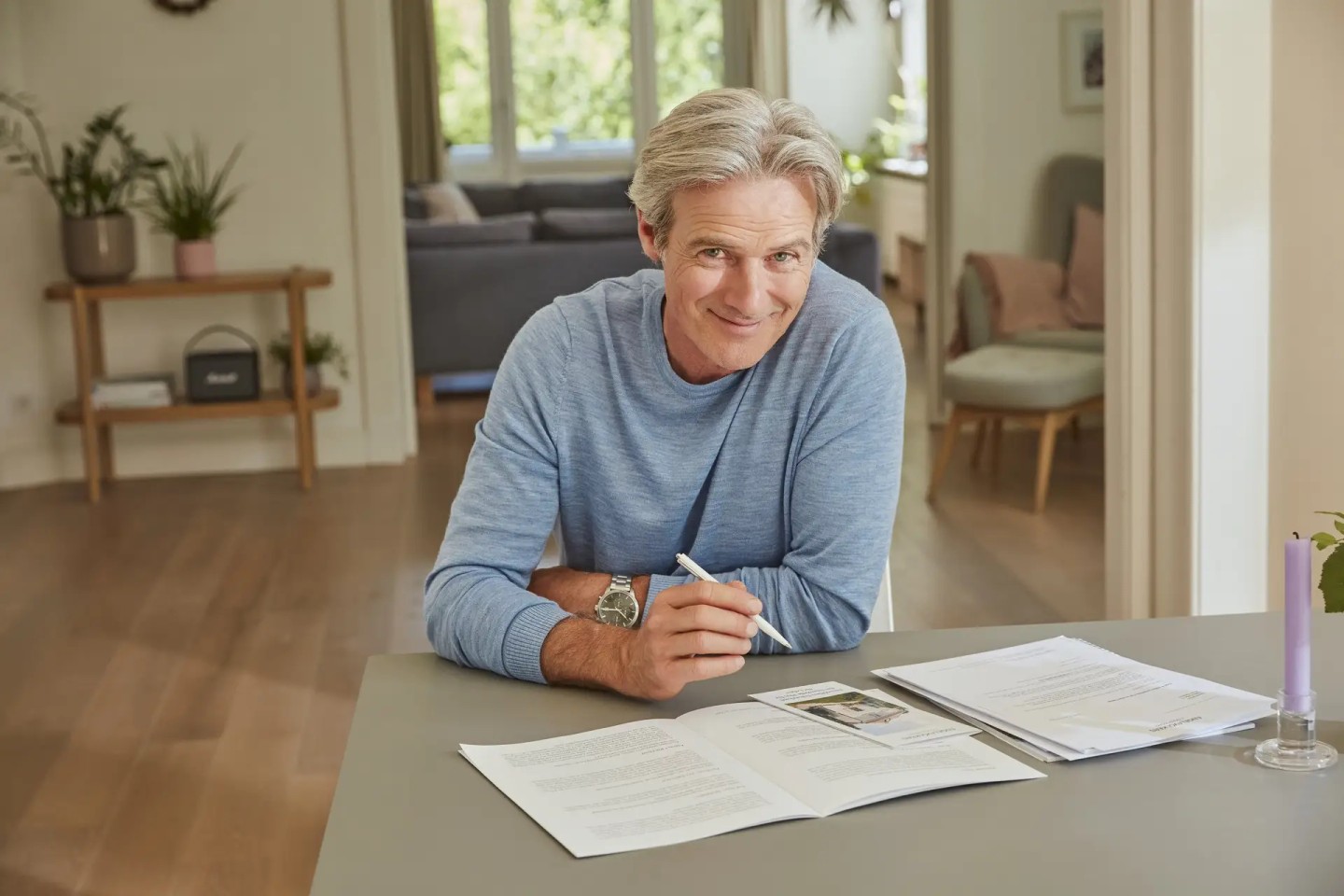 Ein Mann im Rentenalter sitzt an einem Tisch mit einem Stift in der Hand, vor ihm liegen aufgeschlagene Unterlagen.