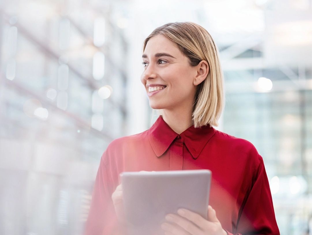 Eine Frau geht einen Gang entlang in einem modernen Büro. Sie lächelt und guckt zur Seite.