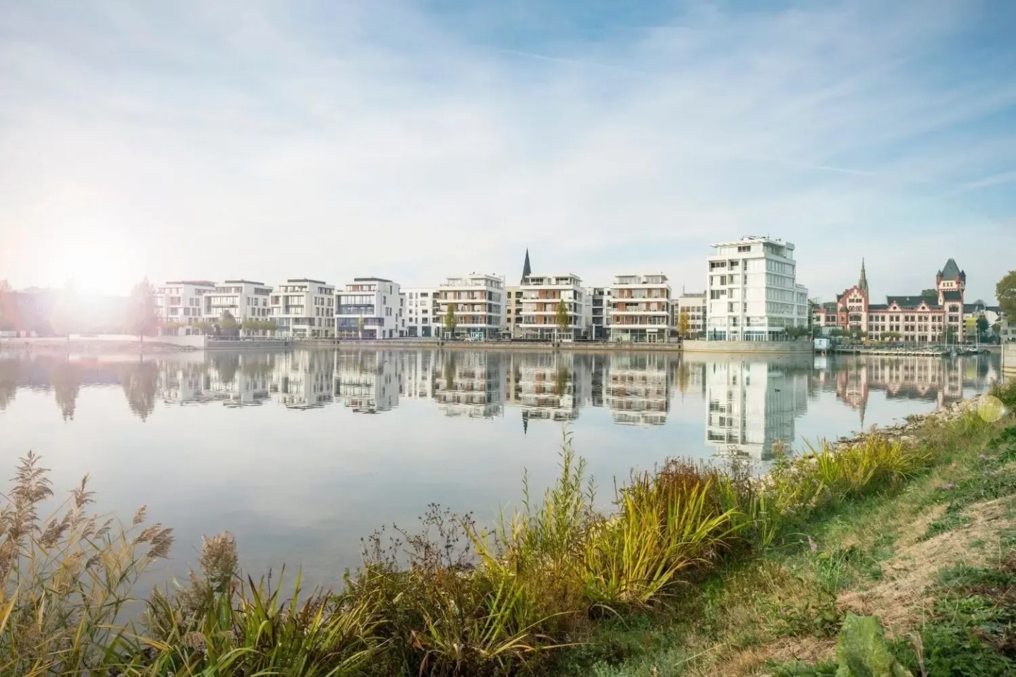Ein Reihe moderne Wohnblocks an einem See mit grünem Ufer.