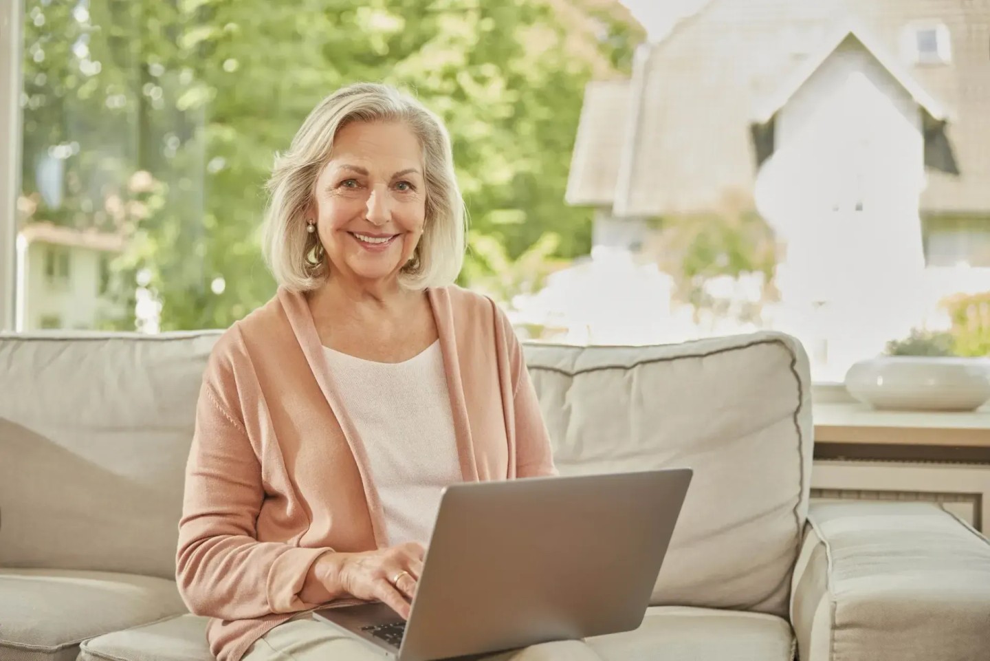 Eine Frau sitzt auf dem Sofa am Laptop. Sie lächelt in d