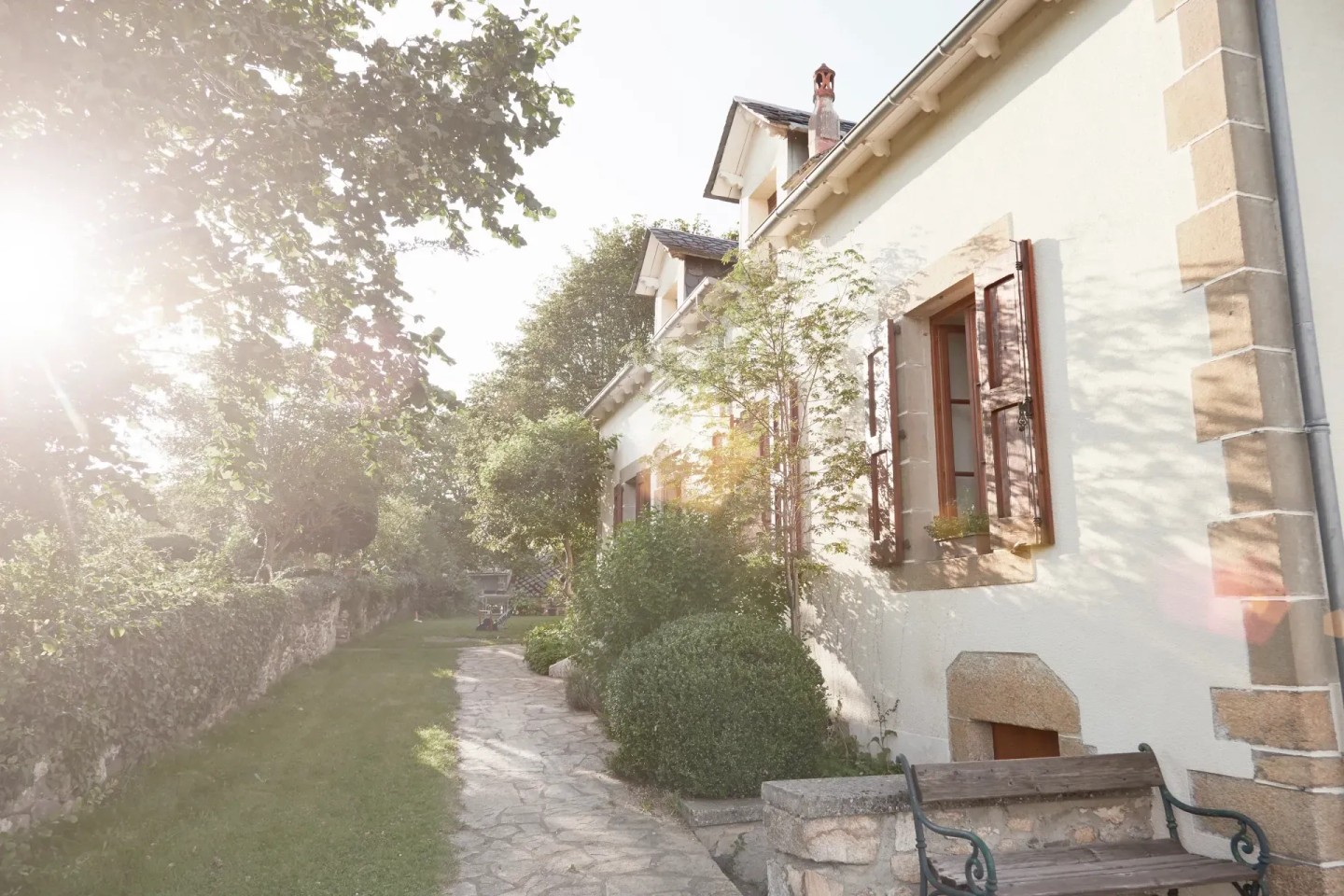 Ein helles Haus von außen, die Sonne scheint durch die Bäume im Garten. Die Eigentümer nutzen die Immobilienverrentung für sich.
