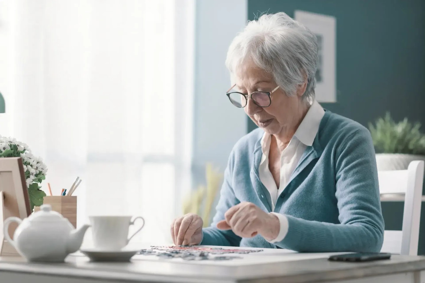 Eine Frau sitzt am Tisch und puzzelt. Sie hält ihr Gehirn fit im Alter.